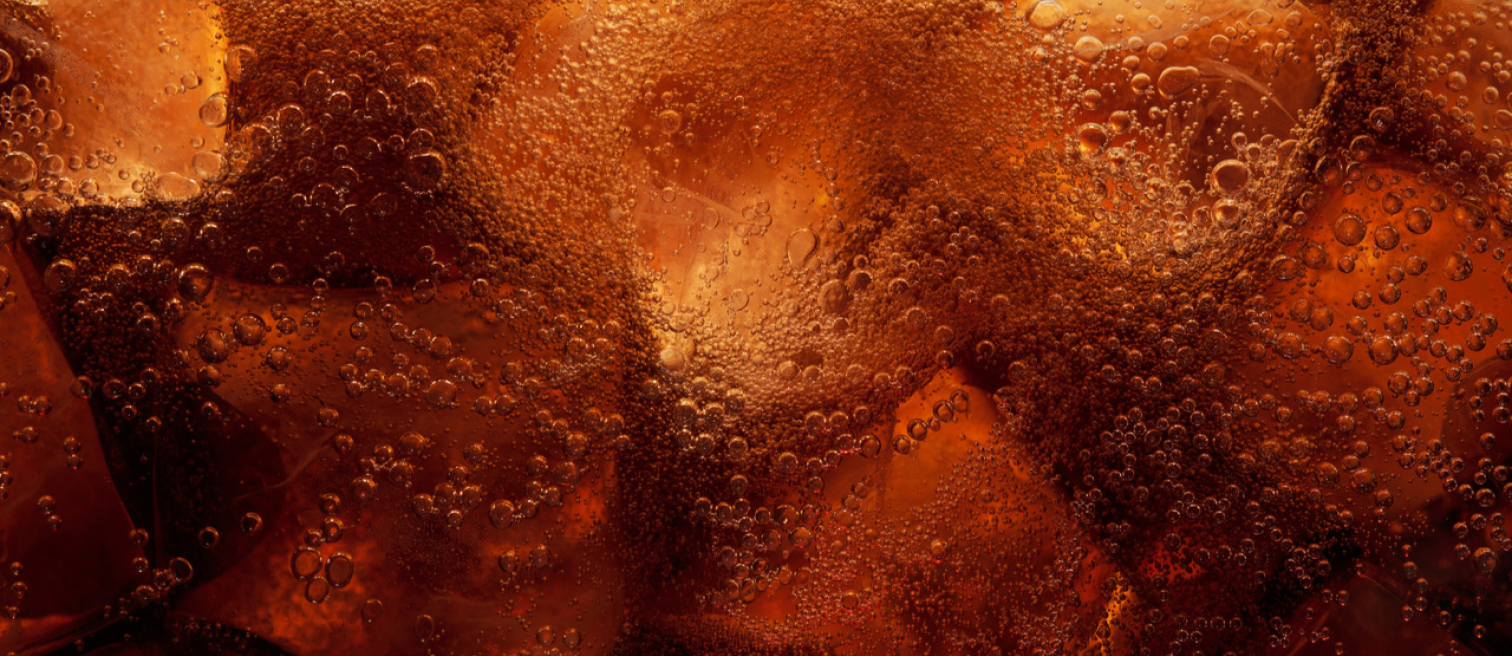 Up close zoomed in image of the dark caramel color liquid from Jack Daniels and Coca-Cola with ice cubes. Carbonation bubbles are present throughout.